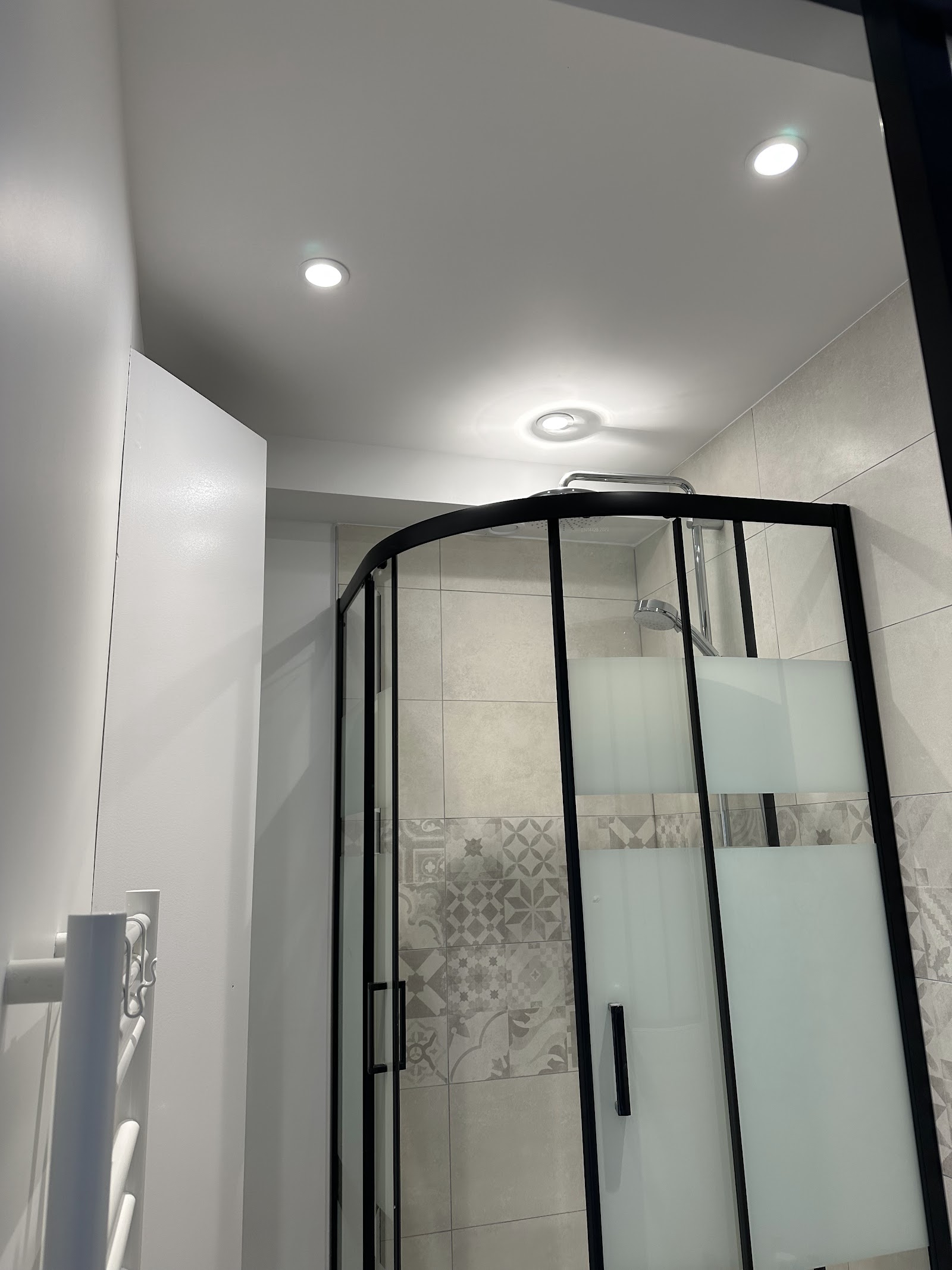 Salle d'eau moderne avec douche à paroi noire et carrelage à motifs géométriques.